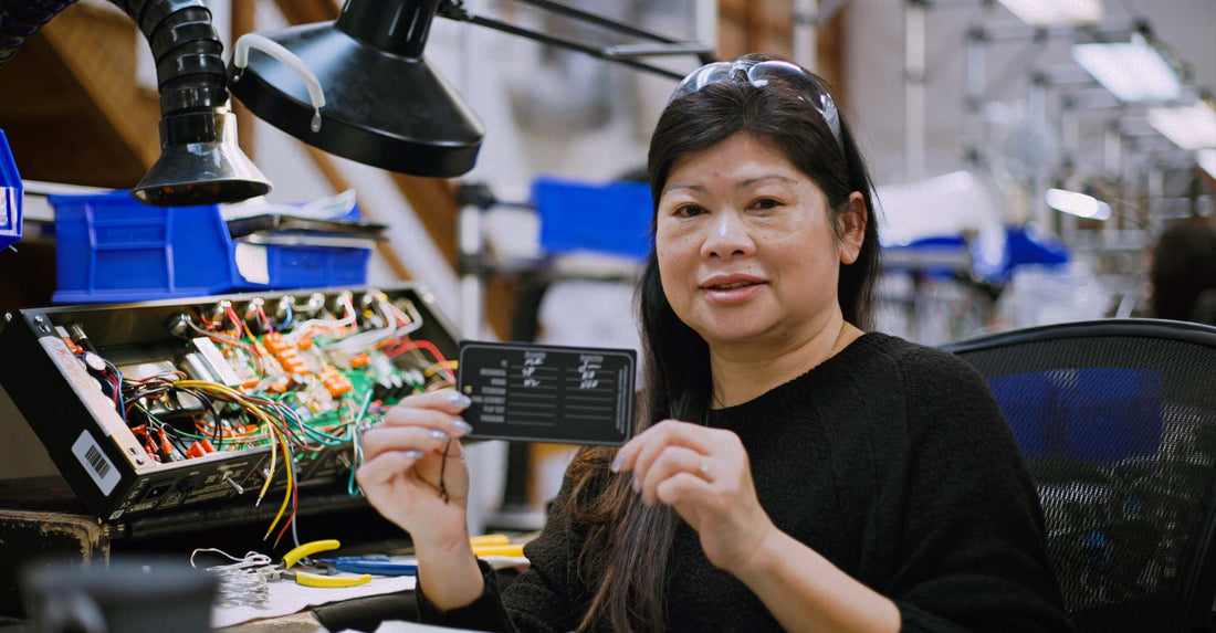 Keo Khamvongsa, mechanical assembly wiring at MESA/Boogie holding up a card while sitting with an amp being made